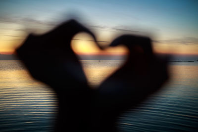 Shadow of person hand on heart shape against sky during sunset