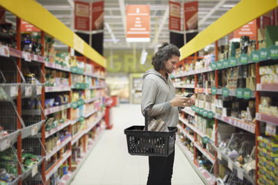 Man in supermarket comparing prices during inflation on cell phone