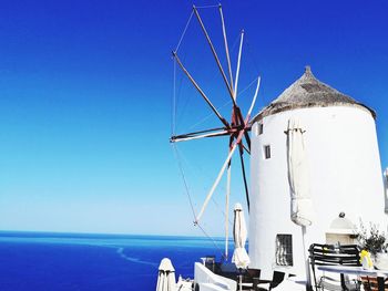 Traditional windmill by sea against clear blue sky