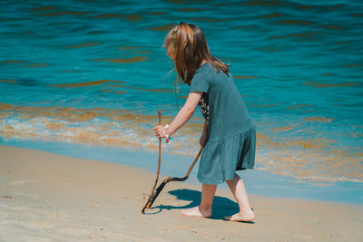 Full length of girl walking while holding sticks at beach against sky