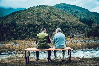 Rear view of couple sitting on mountain against sky