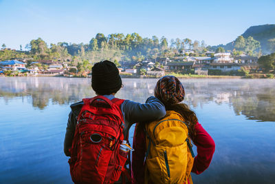 Rear view of people standing by lake against sky