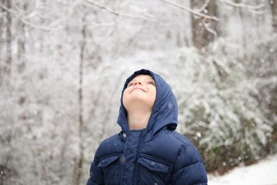 Boy in warm clothing standing against trees