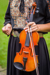 Midsection of woman holding violin while standing on field