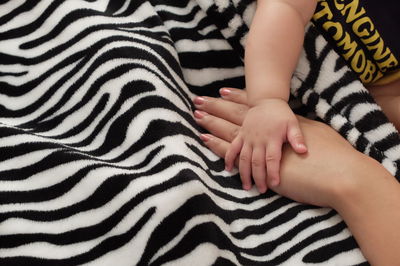 Cropped image of toddler touching mother hand on blanket