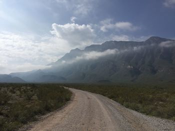 Dirt road leading towards mountains against sky