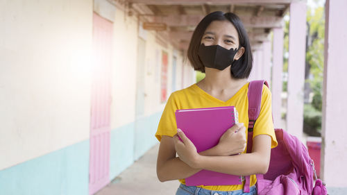 Woman holding book while standing against wall