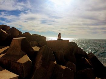 Woman sitting on rocks at shore against sky