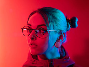 Close-up of young woman wearing eyeglasses while standing red background