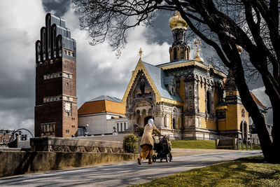 Rear view of woman with baby stroller on road against russian chapel
