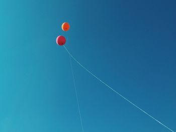 Low angle view of helium balloons against blue clear sky