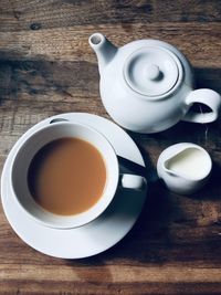 Cool tone background image of a cup of tea with teapot and milk jug in white china on a wooden table