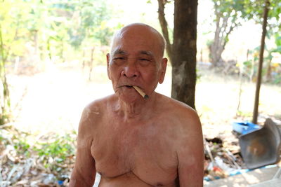 Shirtless senior man smoking cigarette while sitting outdoors