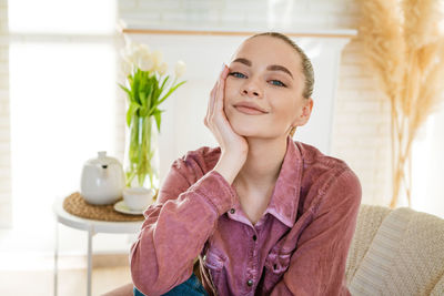 Happy calm young woman relaxing on comfortable armchair in living room, smiling