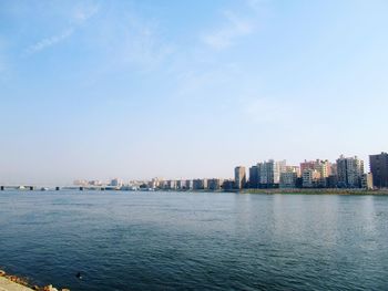 Sea by buildings in city against sky