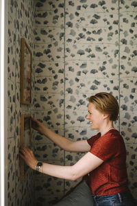 Side view of smiling woman adjusting picture frame on wall at home