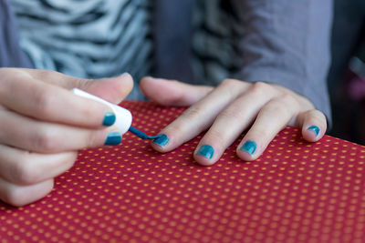 Midsection of woman applying nail polish at table