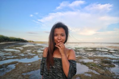 Portrait of young woman eating at beach against sky