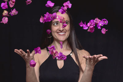 Beautiful mid adult woman throwing flowers against black background
