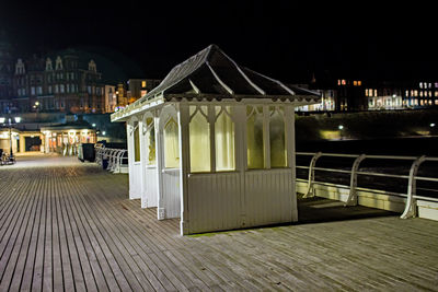 Illuminated footpath by sea against sky in city at night