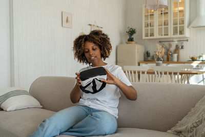 Young woman using phone while sitting on sofa at home