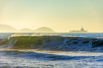 Wave and ship at sunrise with mountains