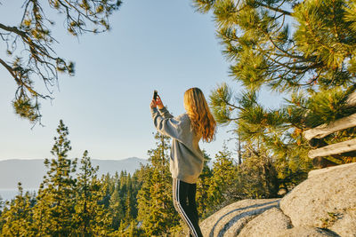 Young woman taking a picture of sunset over lake tahoe.