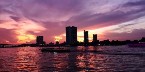 Scenic view of river by buildings against sky during sunset