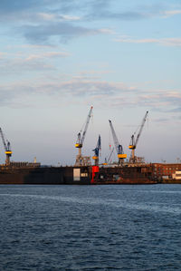 Cranes at commercial dock by sea against sky