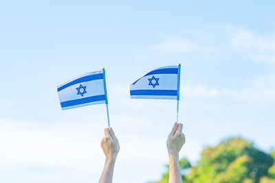 Low angle view of hand holding flag against sky