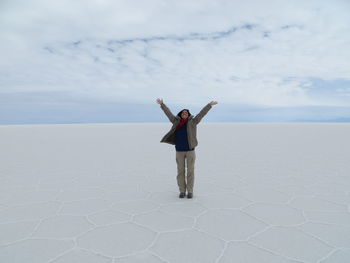 Excited woman standing with arms raised on salt flat at salar de uyuni against sky