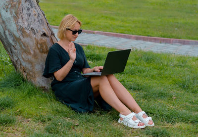 Young woman using laptop while sitting on field