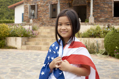 Cute girl with american flag standing against house