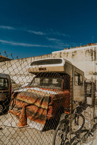Abandoned truck by fence against blue sky