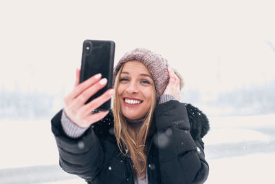 Portrait of smiling young woman using smart phone during winter