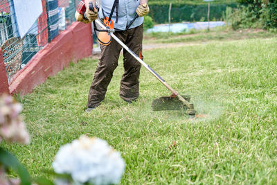 Crop elderly man mowing grass in backyard with lawn mower