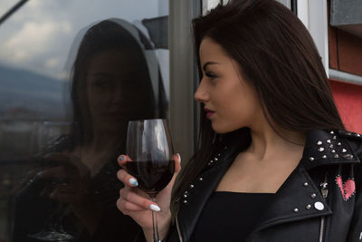 Close-up of young woman holding drink with reflection in glass