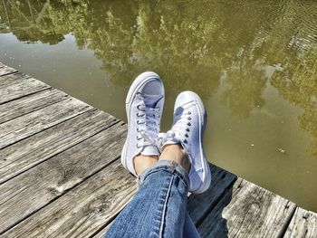 Low section of person wearing white shoes resting on pier over lake