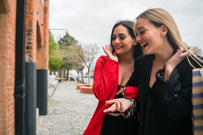 Smiling young women holding shopping bag standing outdoors