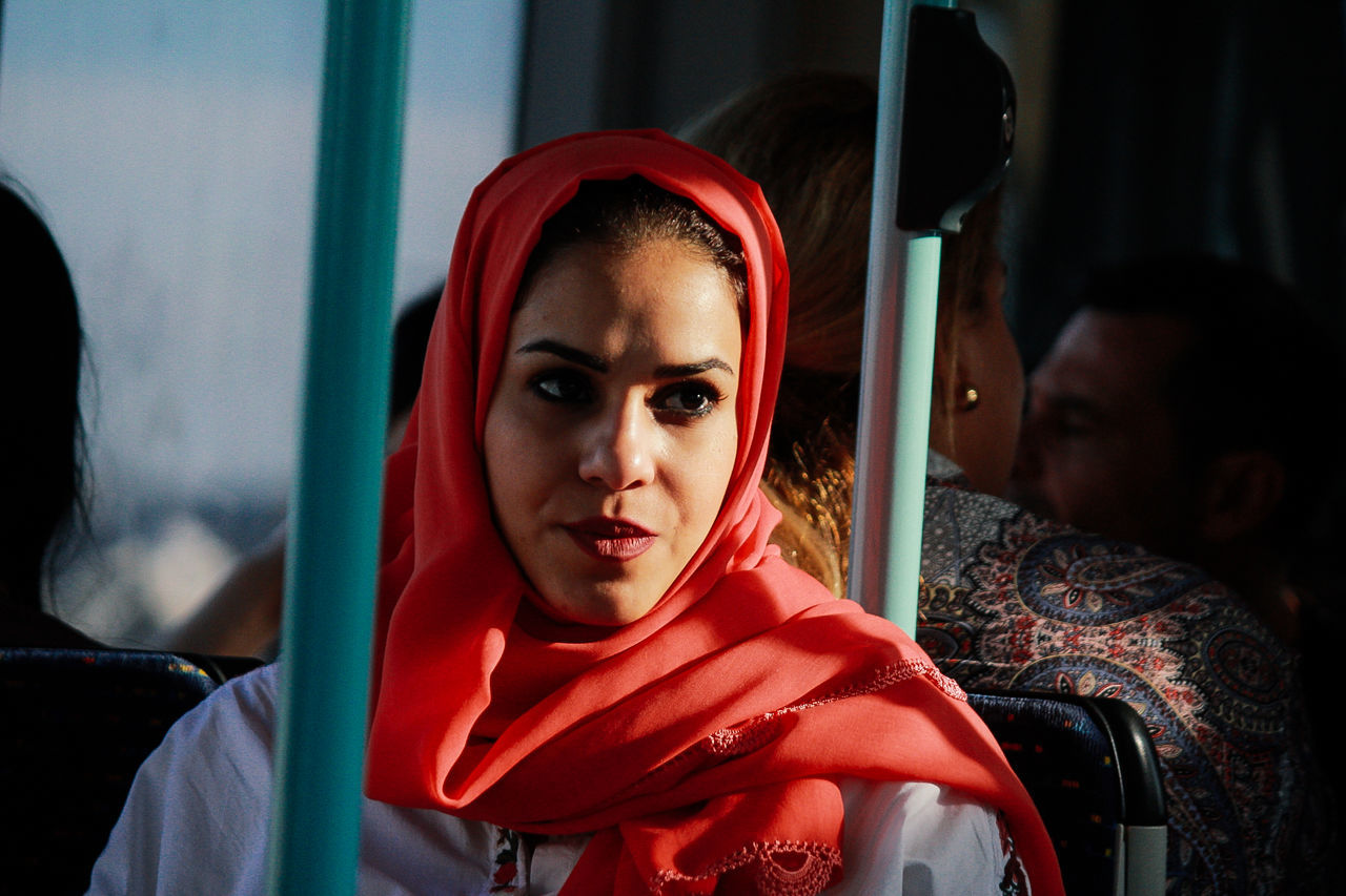 real people, young adult, lifestyles, portrait, young women, headshot, leisure activity, vehicle interior, mode of transportation, red, front view, people, transportation, looking, public transportation, sitting, looking at camera, young men, traditional clothing, land vehicle