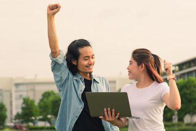 Happy young woman using mobile phone against sky