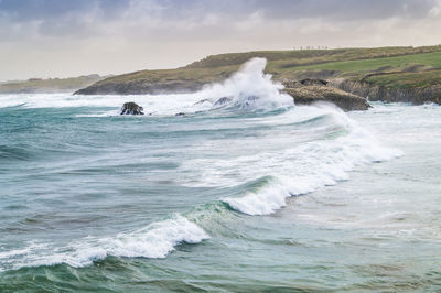 Scenic view of sea waves crashing at shore against sky