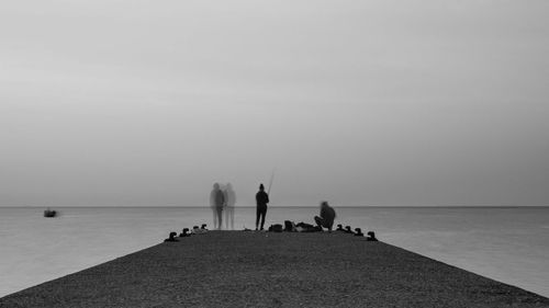 People fishing on pier in sea against sky