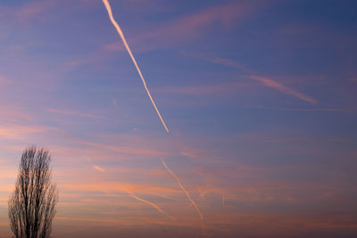 Low angle view of vapor trails in sky at sunset