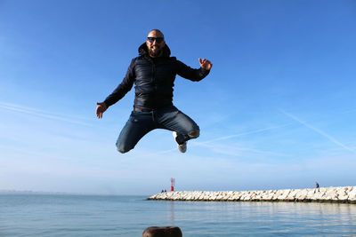 Full length of man jumping over sea against blue sky