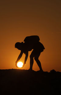 Optical illusion of silhouette woman holding sun during sunset