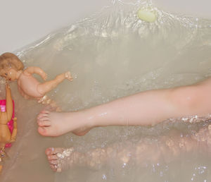 High angle view of child and plastic doll swimming in bath