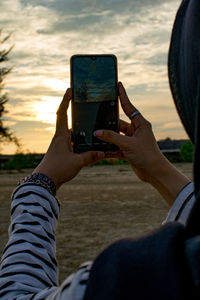 Midsection of woman photographing sunset 