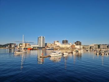 Buildings by sea against clear blue sky