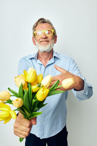 Portrait of senior man holding yellow flower against white background